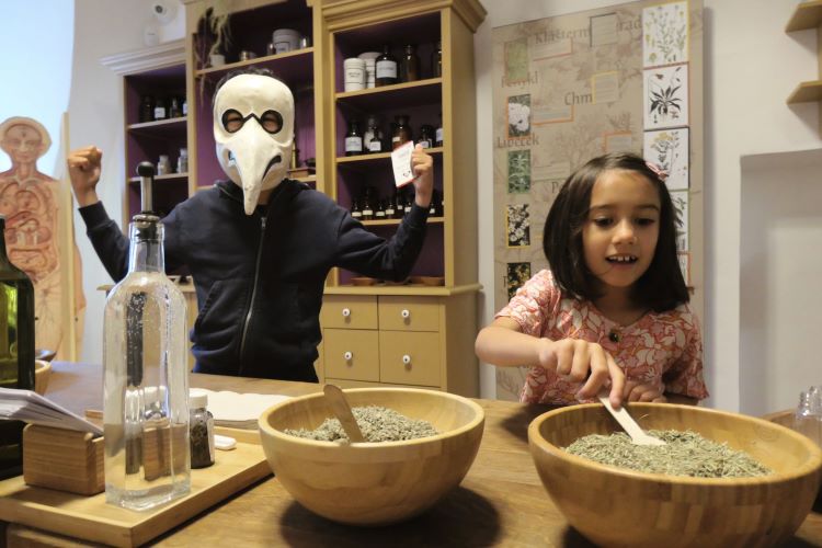 Girl mixing potions at 3+ gallerie in Cesky Krumlov. Boy wearing old fashioned plague mask with hooked beak. Things to do with kids in Cesky Krumlov with kids