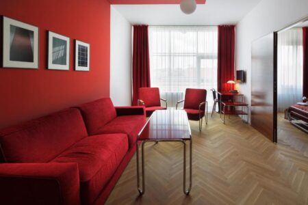 Family suite at AXA Hotel featuring a bedroom and a sperate living area. The living area has ruby red walls, retro furniture and a large sofa. One of the best family-friendly hotels in Prague - The Little Adventurer