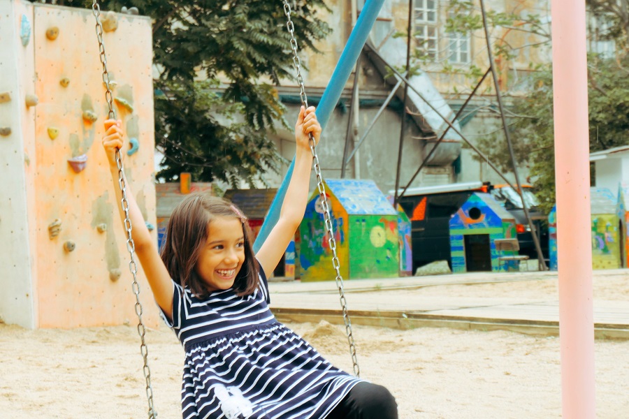 Child playing on a swing at the playground at Kasarna Karlin Prague. Also in sight is a large sand pit, climbing structure and colourful play huts. One of the things to do in Prague with kids