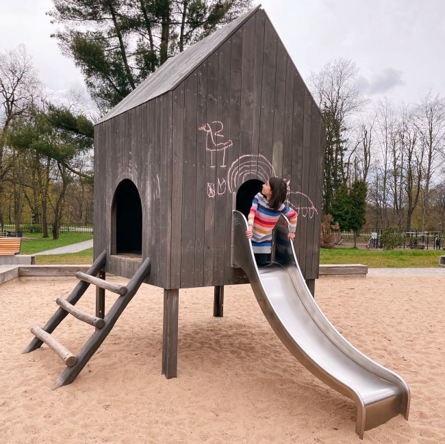 Child playing in a small wooden house with a slide into a large sandpit in Stromovka Prague